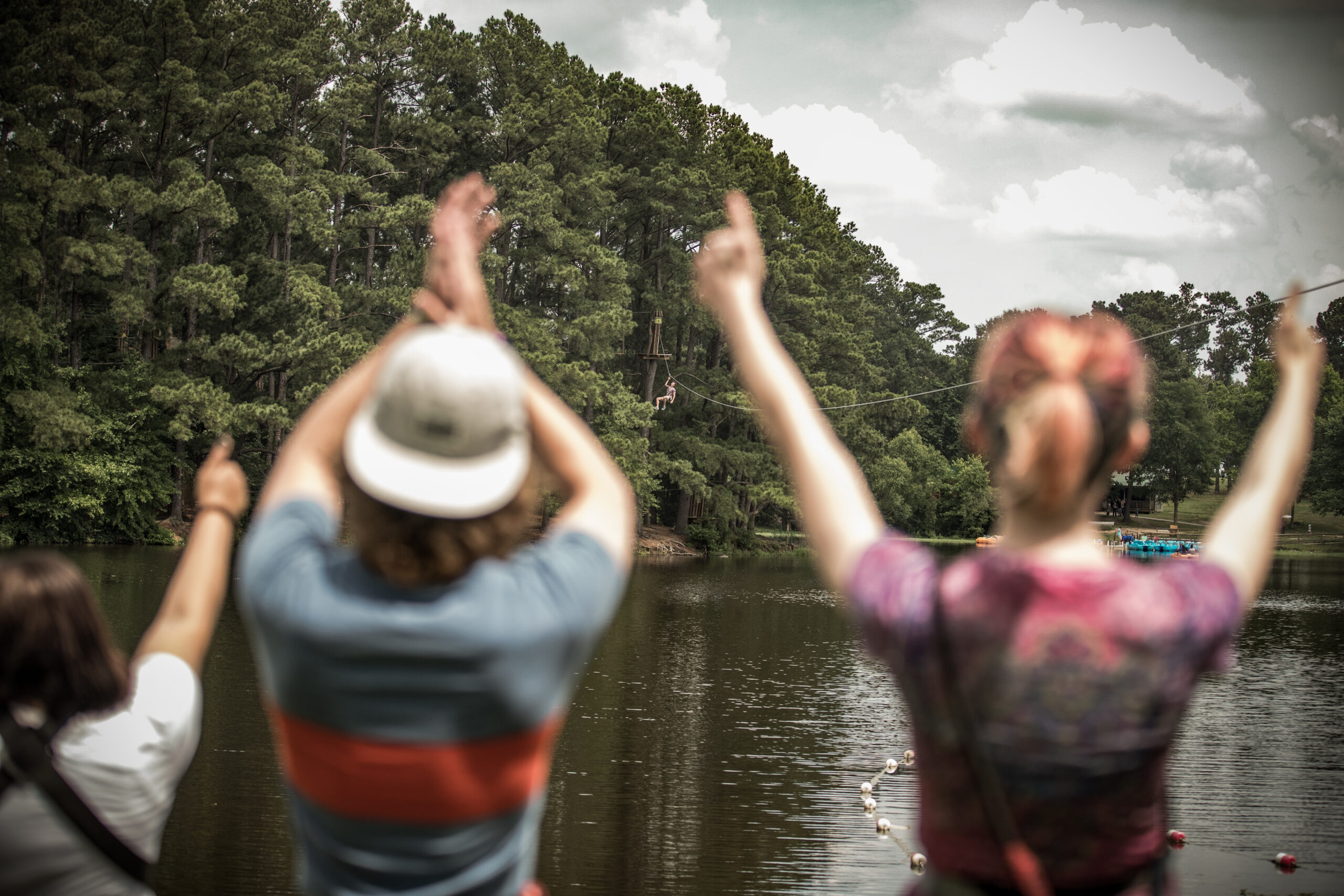 Young adults cheering on a teammate ziplining across a pond