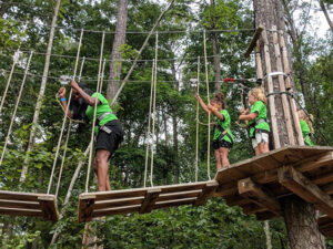 A camp counselor being cheered on by campers as she crosses a treetop bridge in Williamsburg, Virginia